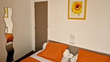 Une chambre d’hôtel avec un lit, une literie orange, une porte, un interrupteur fixé au mur et un tableau représentant une fleur.