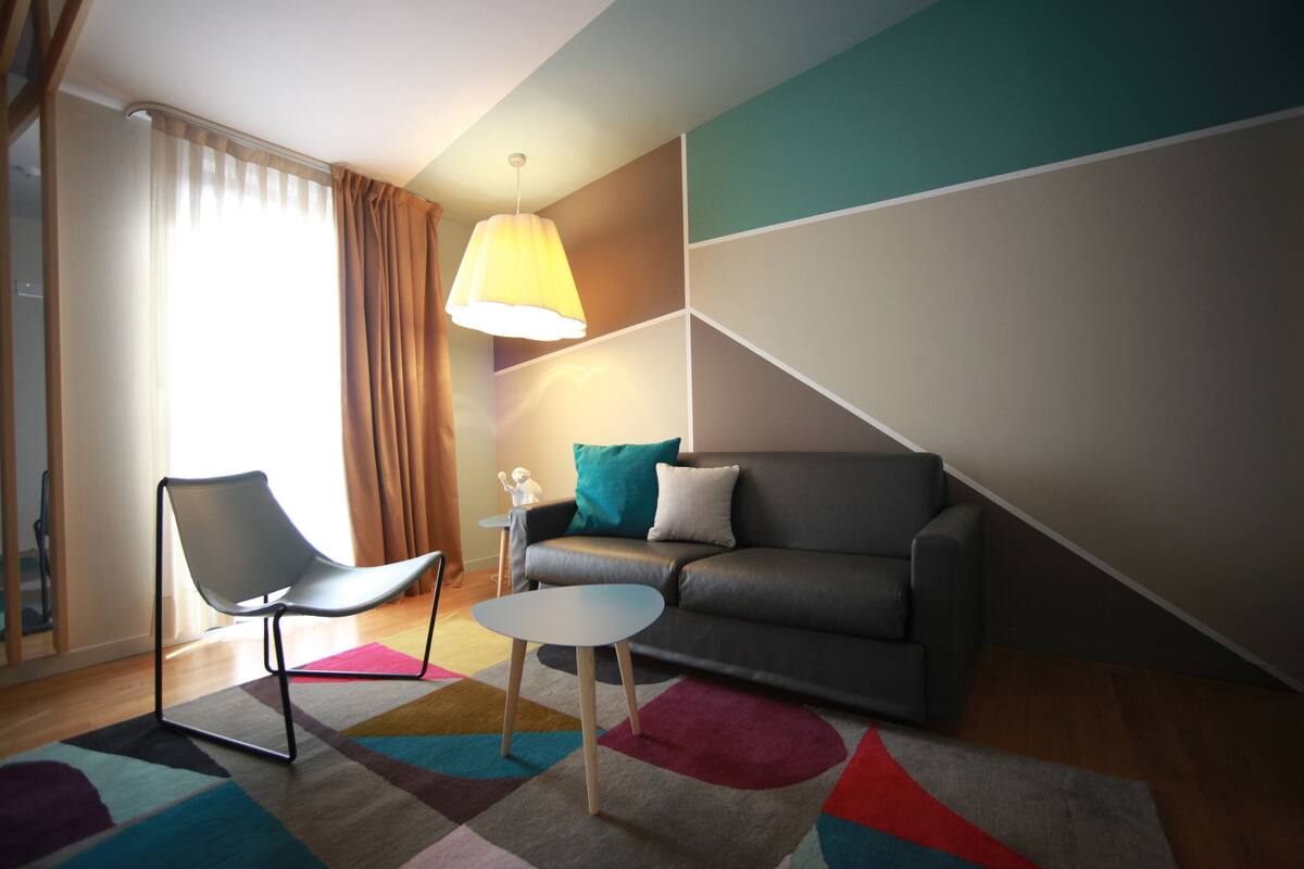 A modern living room with a sofa, a chair, a small table, and a colorful rug.