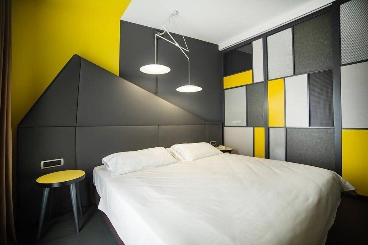 A modern hotel room with a bed, a small table, and a unique geometric wall design.