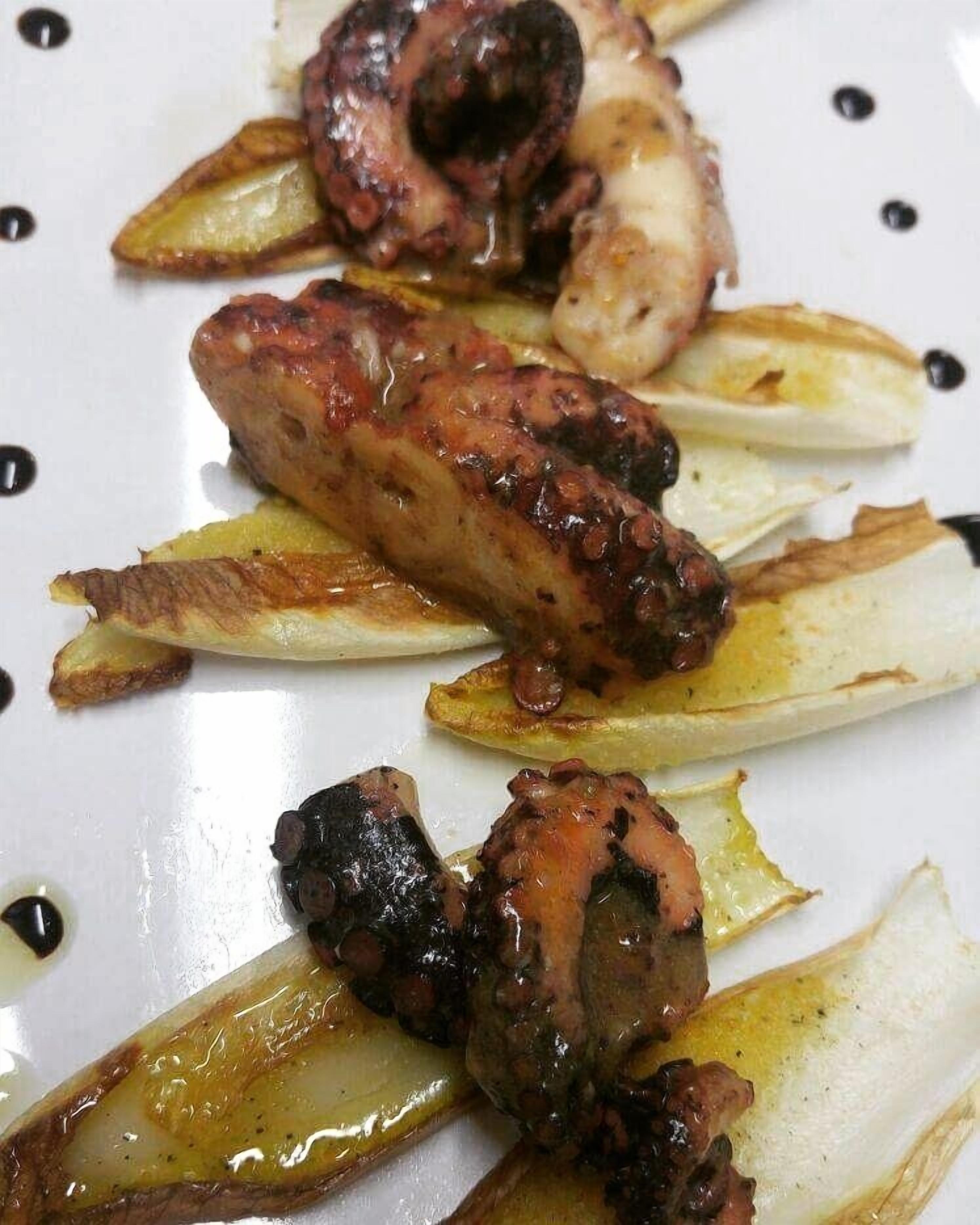 Un plato de pulpo a la parrilla con rodajas de limón y salsa oscura.