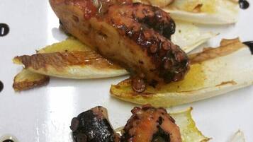 Un plato de pulpo a la parrilla con rodajas de limón y salsa oscura.