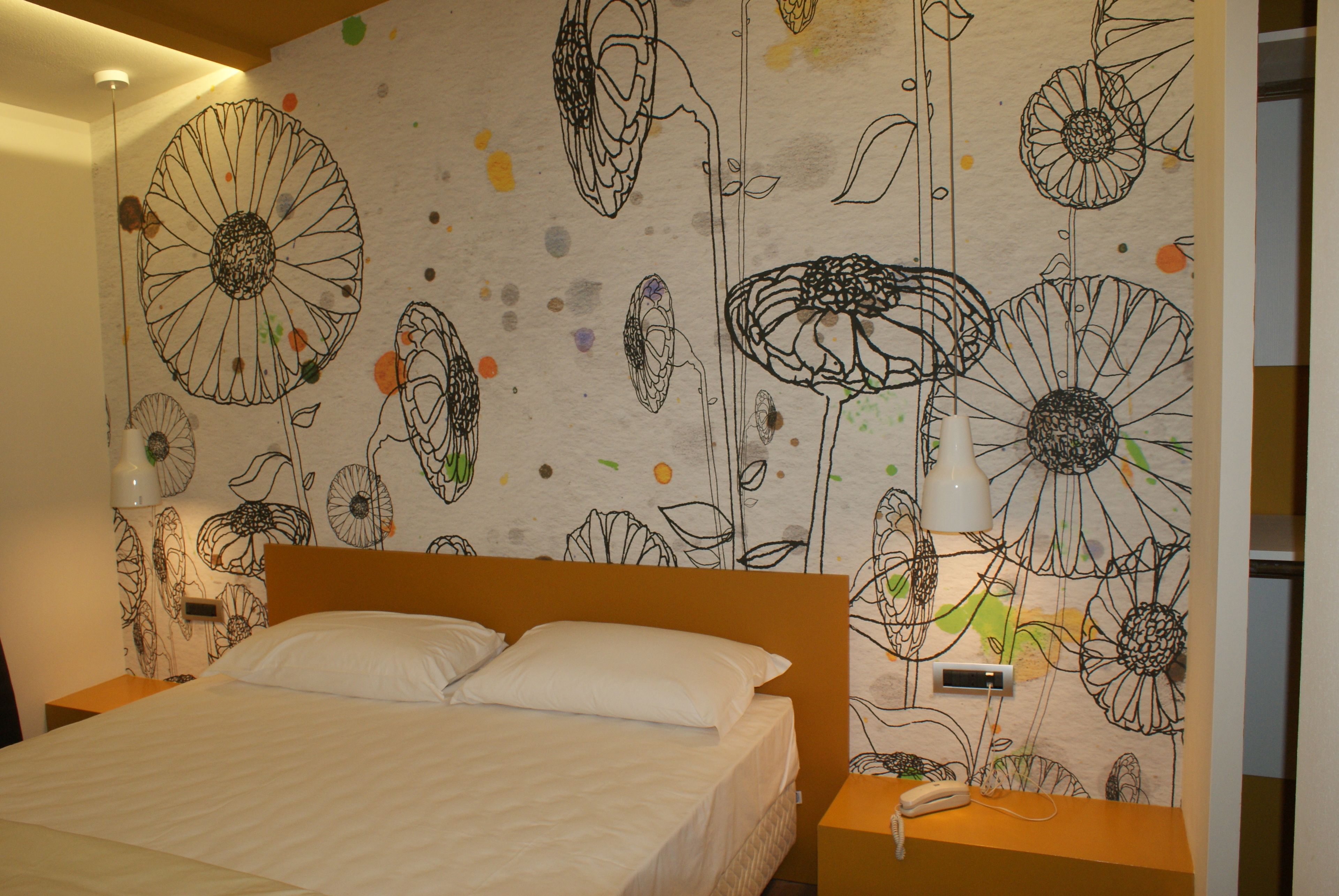A bedroom with a bed, a nightstand, and a wall with floral patterns.