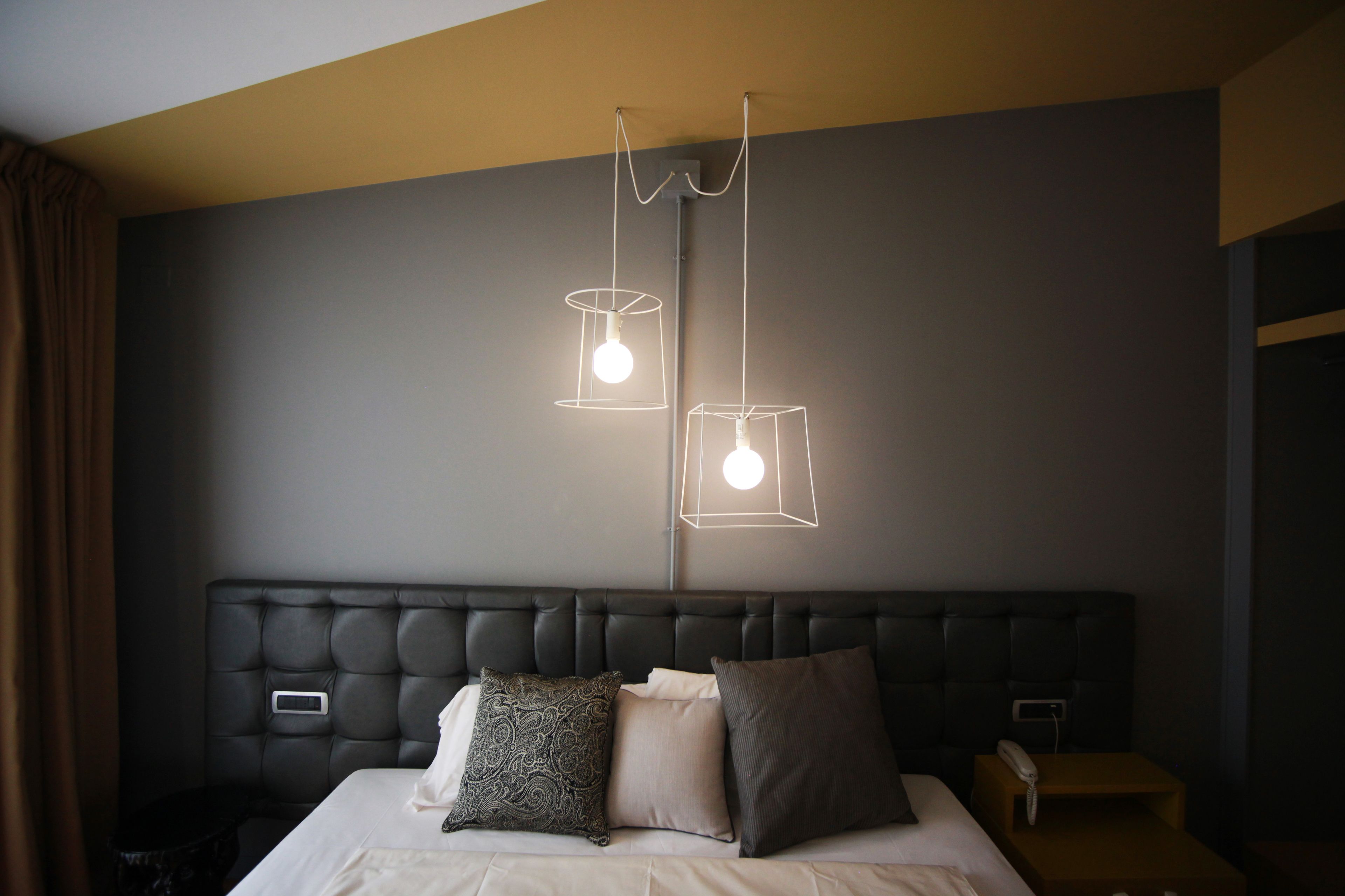 A modern hotel room with a tufted headboard, a bed with three pillows, and two pendant lights.