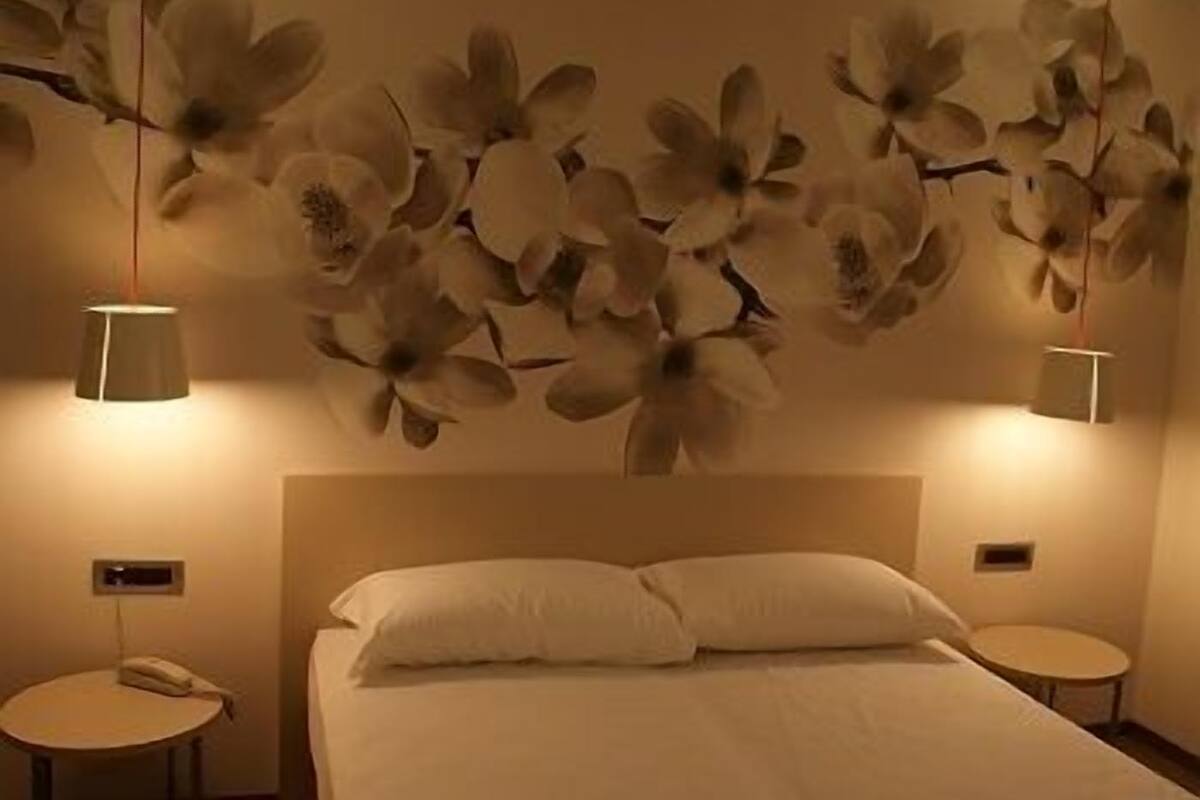 A bedroom with a large bed, two bedside tables, a wall-mounted lamp, and a wall decoration of flowers.
