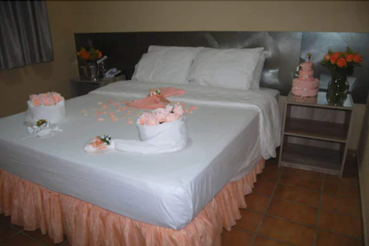 A neatly made bed with white linens, a pink skirt, and a bouquet of flowers.