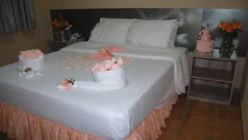 A neatly made bed with white linens, a pink skirt, and a bouquet of flowers.