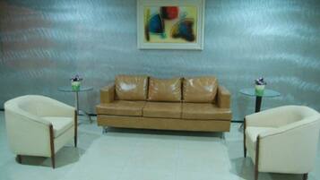 Una habitación con un sofá de cuero marrón, dos sillones blancos, una mesa de centro de vidrio y un cuadro en la pared.