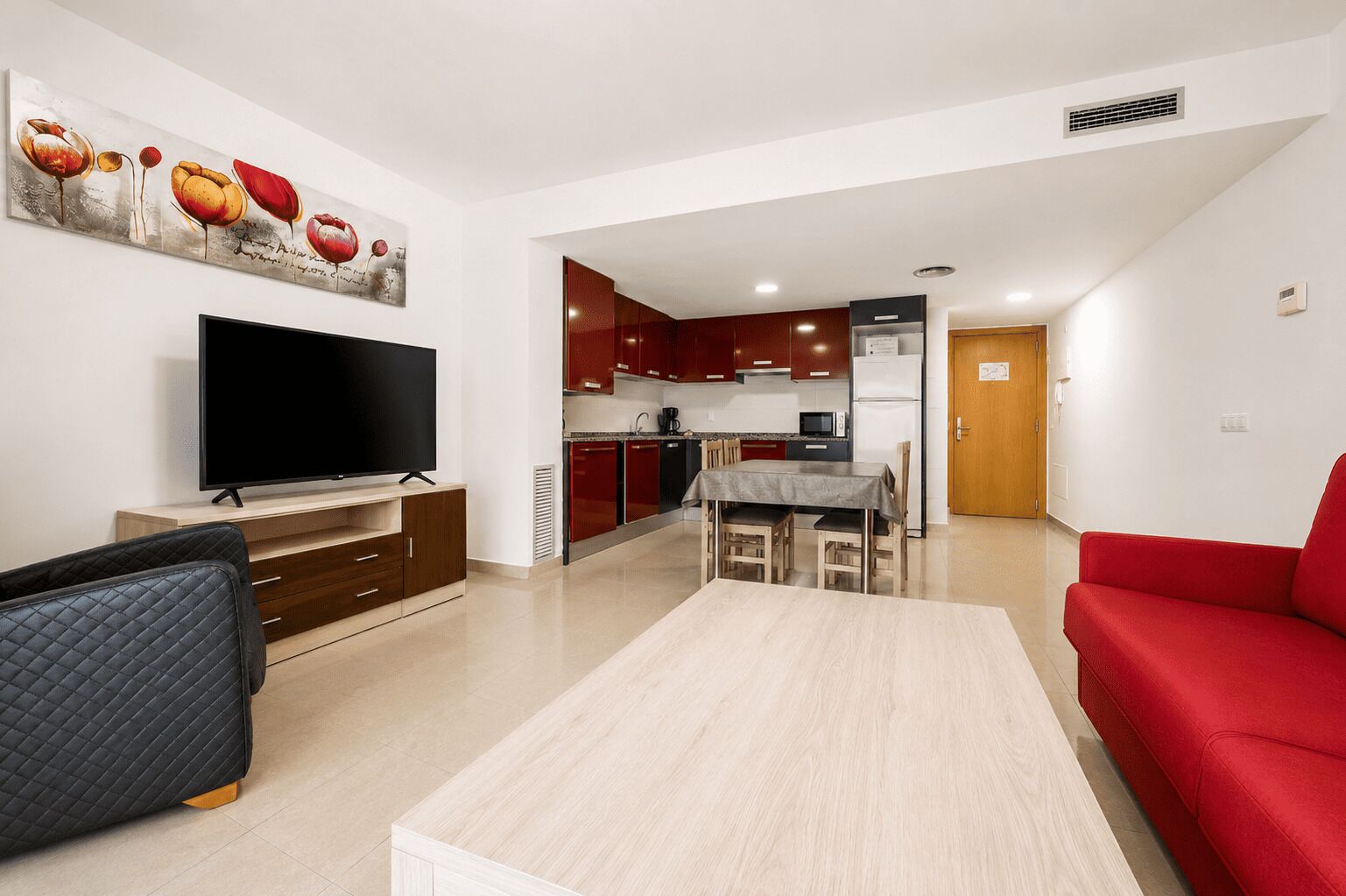 Un salon moderne doté d’un téléviseur à écran plat, d’un canapé rouge, d’un fauteuil noir et d’un coin repas avec une table et des chaises.