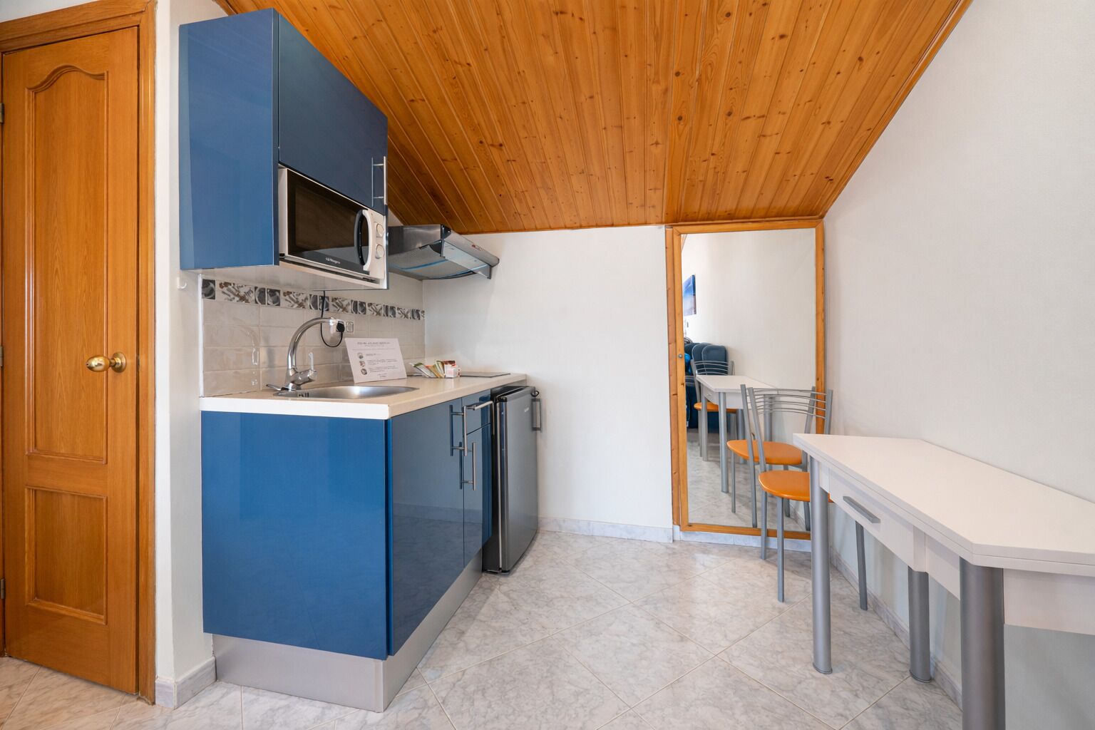 Une cuisine compacte avec des meubles bleus, un four à micro-ondes et un évier. On y trouve également un coin repas avec une table et des chaises.