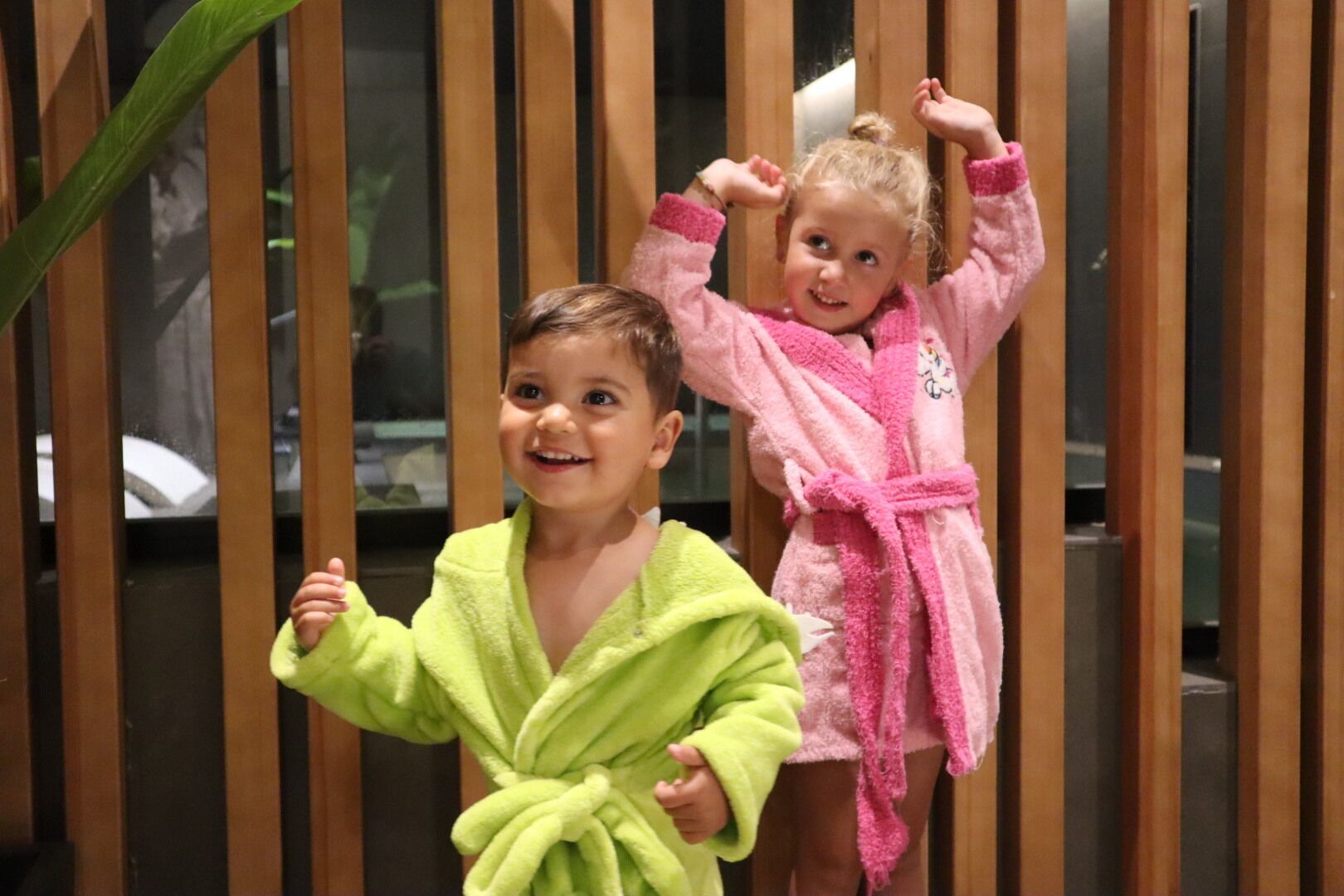 Dos niños con batas de baño frente a una mampara de madera.