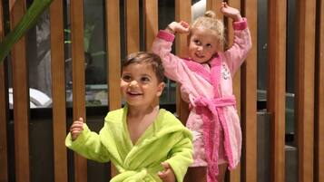 Dos niños con batas de baño frente a una mampara de madera.