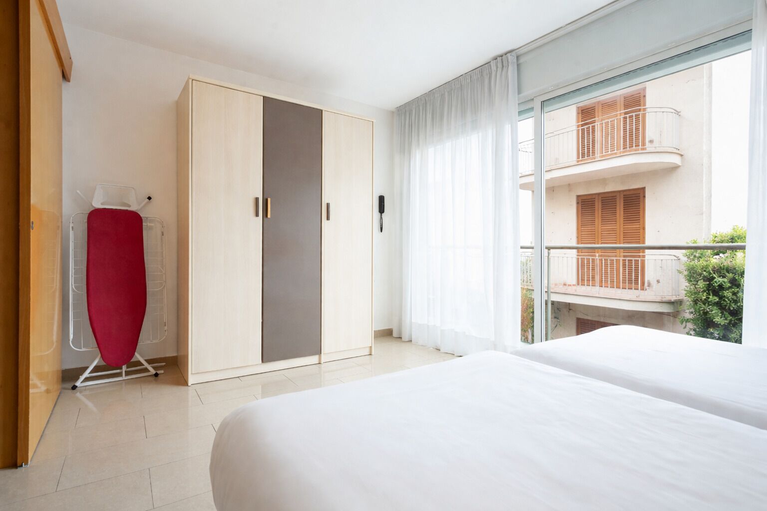 A hotel room with a bed, a wardrobe, an ironing board, and a balcony with a view.