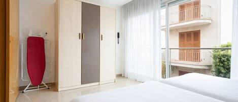 A hotel room with a bed, a wardrobe, an ironing board, and a balcony with a view.