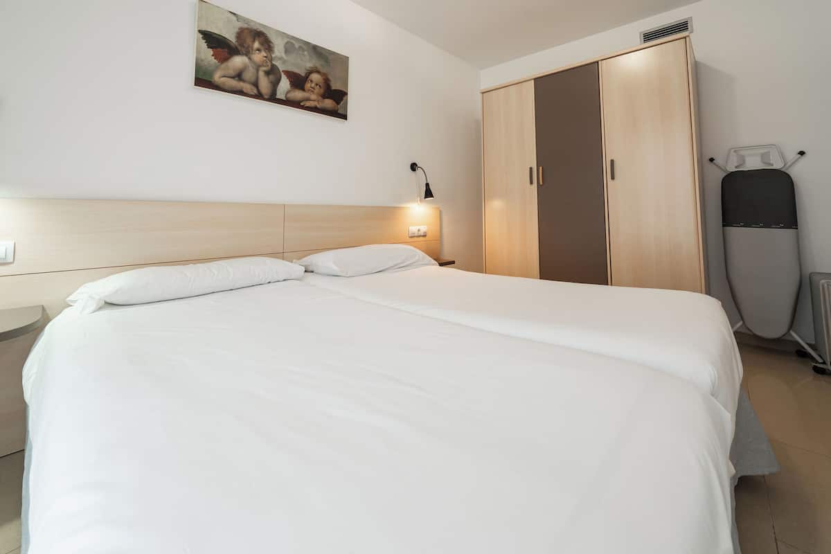 Cama bem arrumada com lençóis brancos em quarto de hotel, guarda-roupa de madeira, quadro na parede e aquecedor.