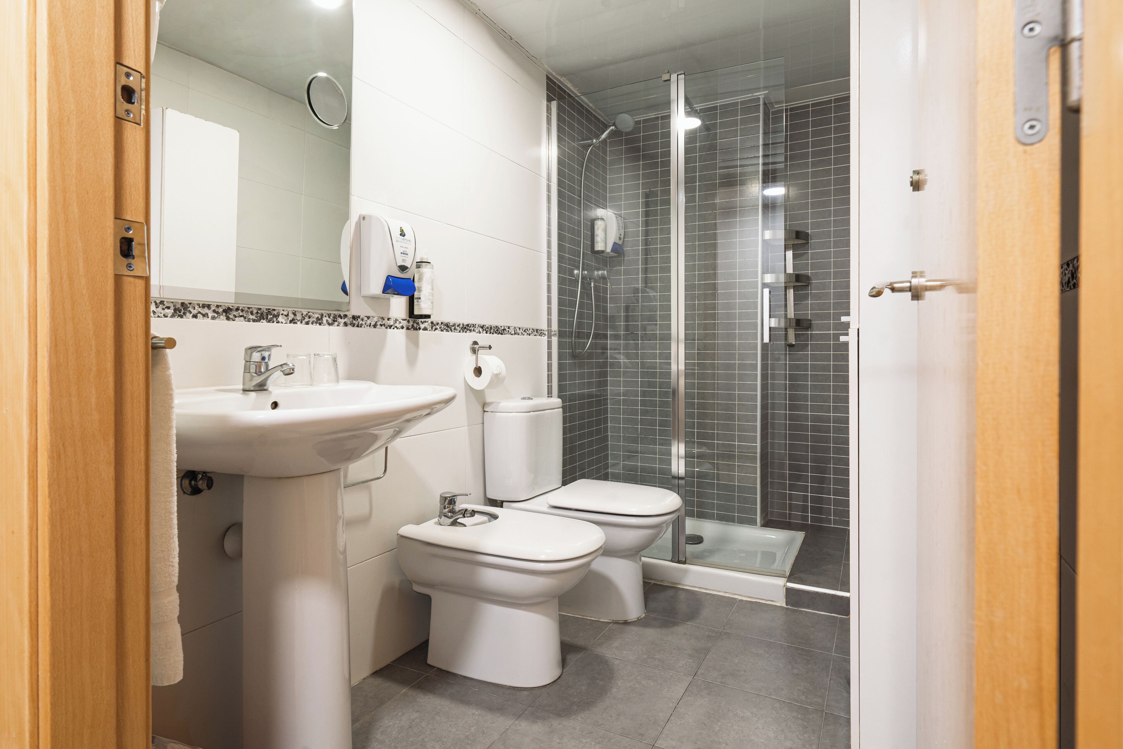 Ein modernes Badezimmer mit Waschbecken, zwei Toiletten, einer Dusche und einem Spiegel.