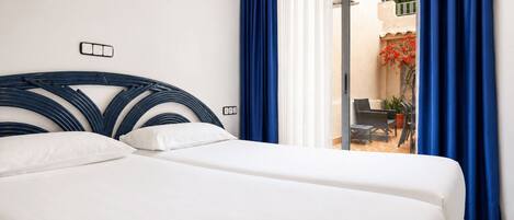 Habitación de hotel con cama, ventana con cortinas azules y vista a un espacio exterior.