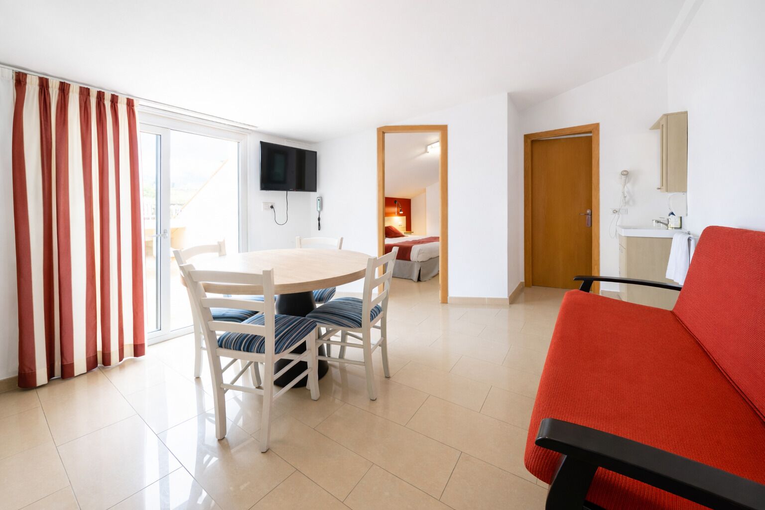 Una sala de estar moderna con comedor, un sofá rojo y un televisor montado en la pared.