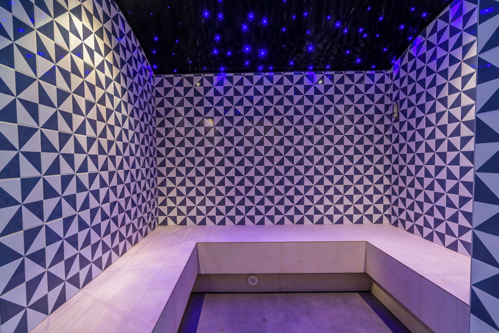 A room with a geometric patterned wall, a small seating area, and a ceiling with star-like lights.