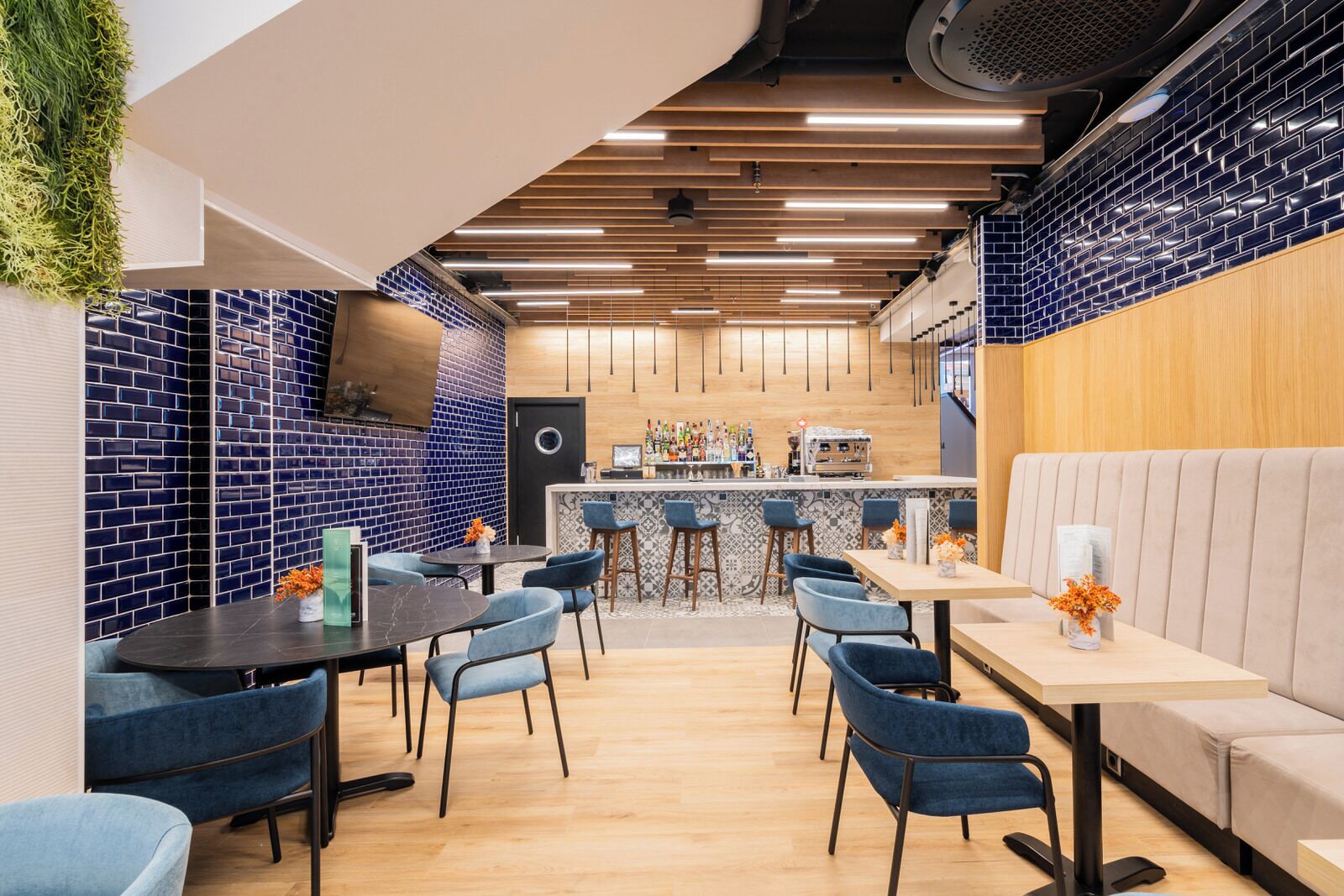 A modern restaurant with blue-tiled walls, wooden ceiling panels, and a bar area.