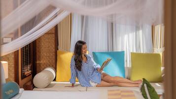 A person sitting on a bed with a book, in a room with a canopy bed and colorful pillows.