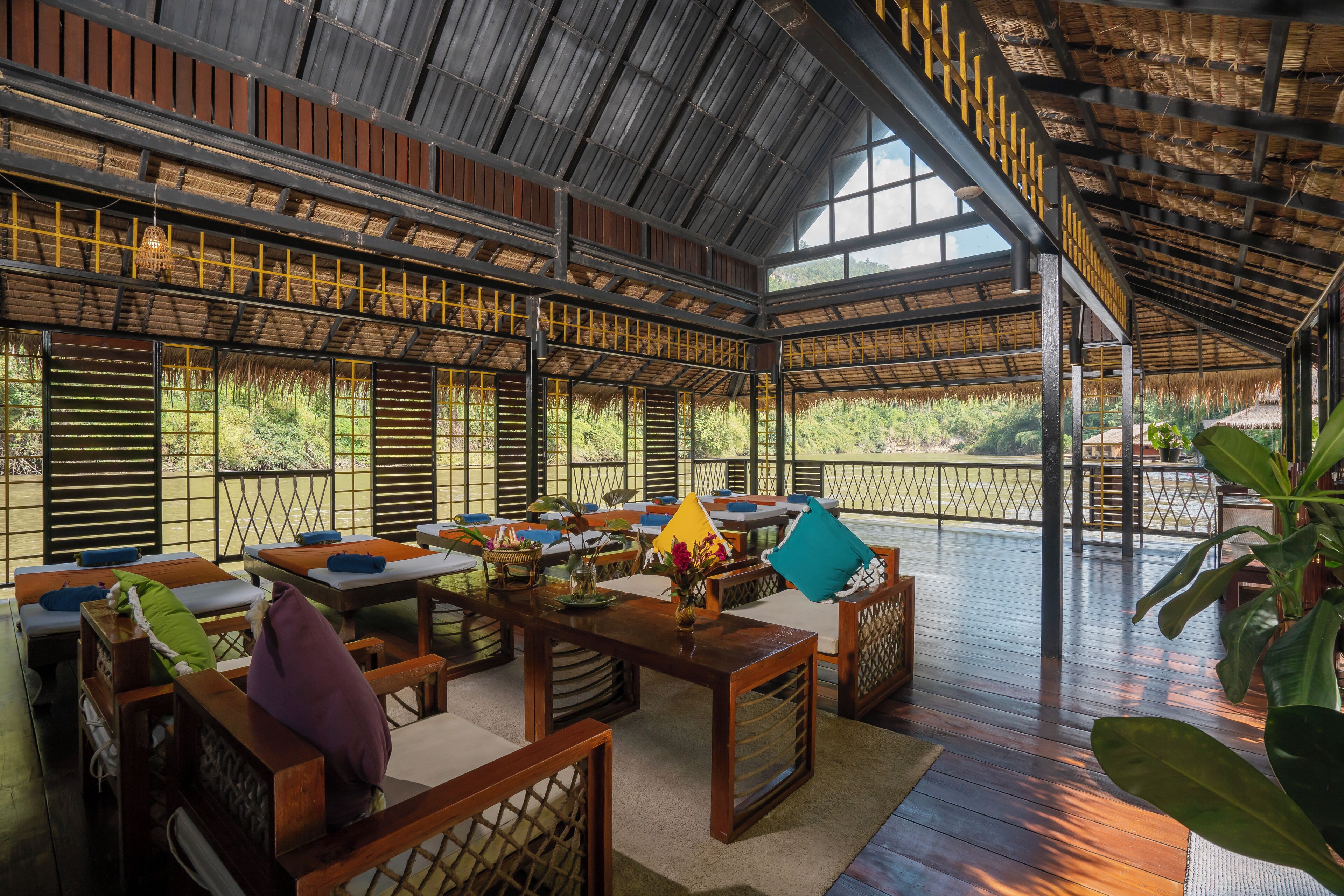 Un espacio interior con asientos de madera, una mesa con un jarrón de flores y vistas a la vegetación exterior.