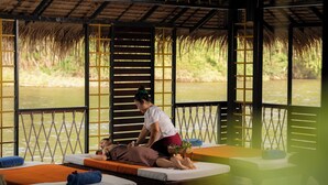 Ein Massageroom mit Blick auf einen Fluss, Holzbetten und einem Strohdach.
