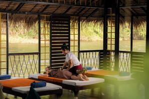 Un cuarto de masoterapia con vista al río, camas de madera y techo de paja.