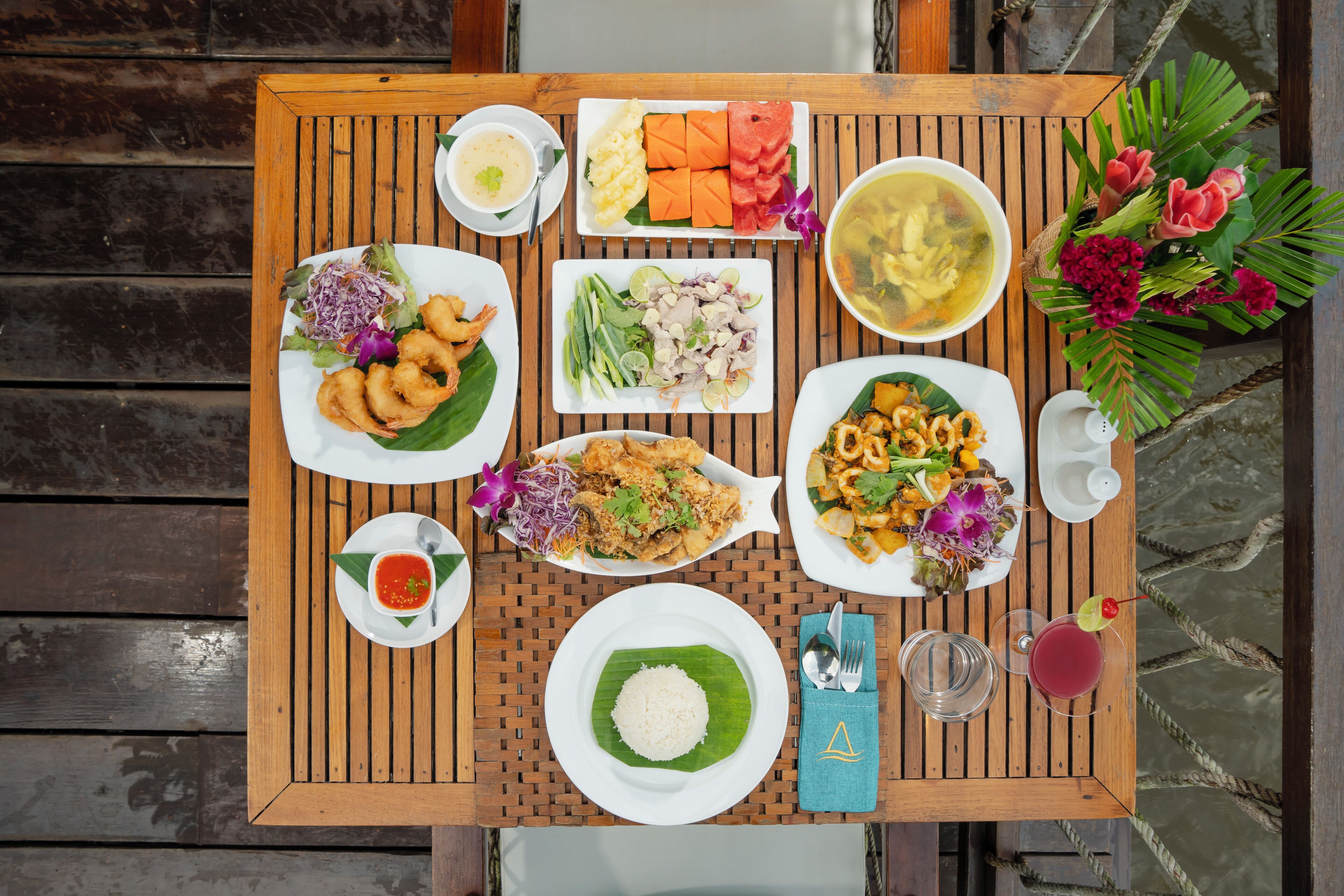 A wooden table with various dishes, including rice, salad, and soup, arranged for a meal.