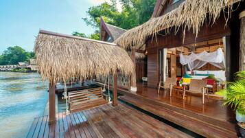 A wooden deck with a thatched roof, overlooking a body of water.