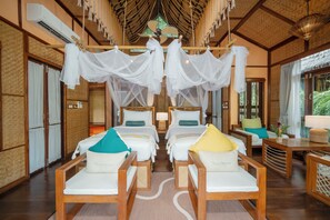 A hotel room with four beds, each with a canopy, wooden furniture, and a view of greenery outside. - The FloatHouse River Kwai (Sai Yok)