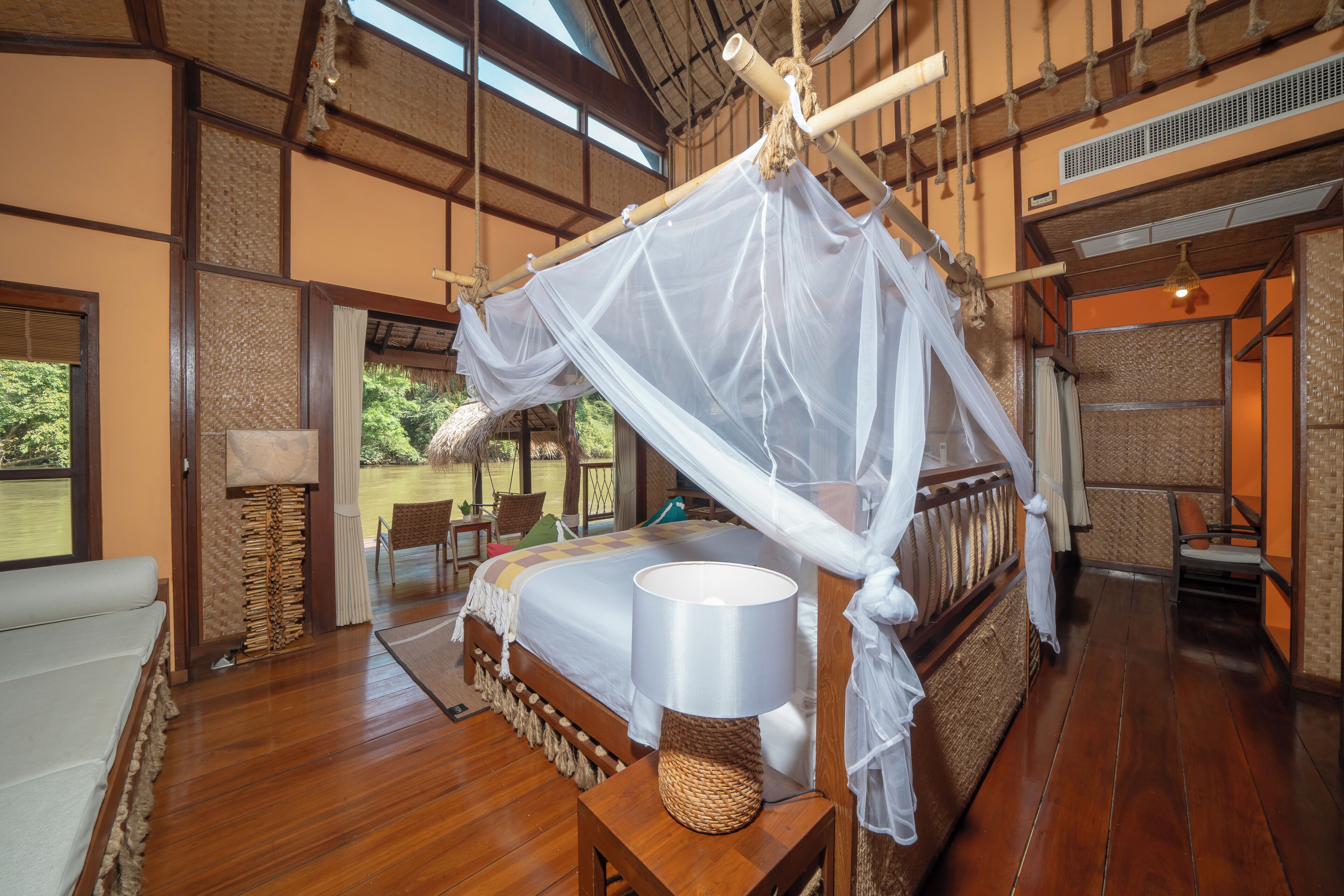 A room with a bed under a canopy, a wooden floor, and a view of the outdoors.