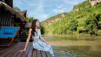 A person sitting on a wooden deck with a view of a river and a forested hillside.