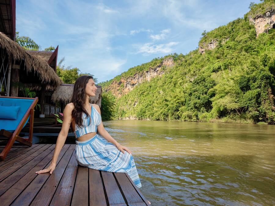 A person sitting on a wooden deck with a view of a river and a forested hillside.