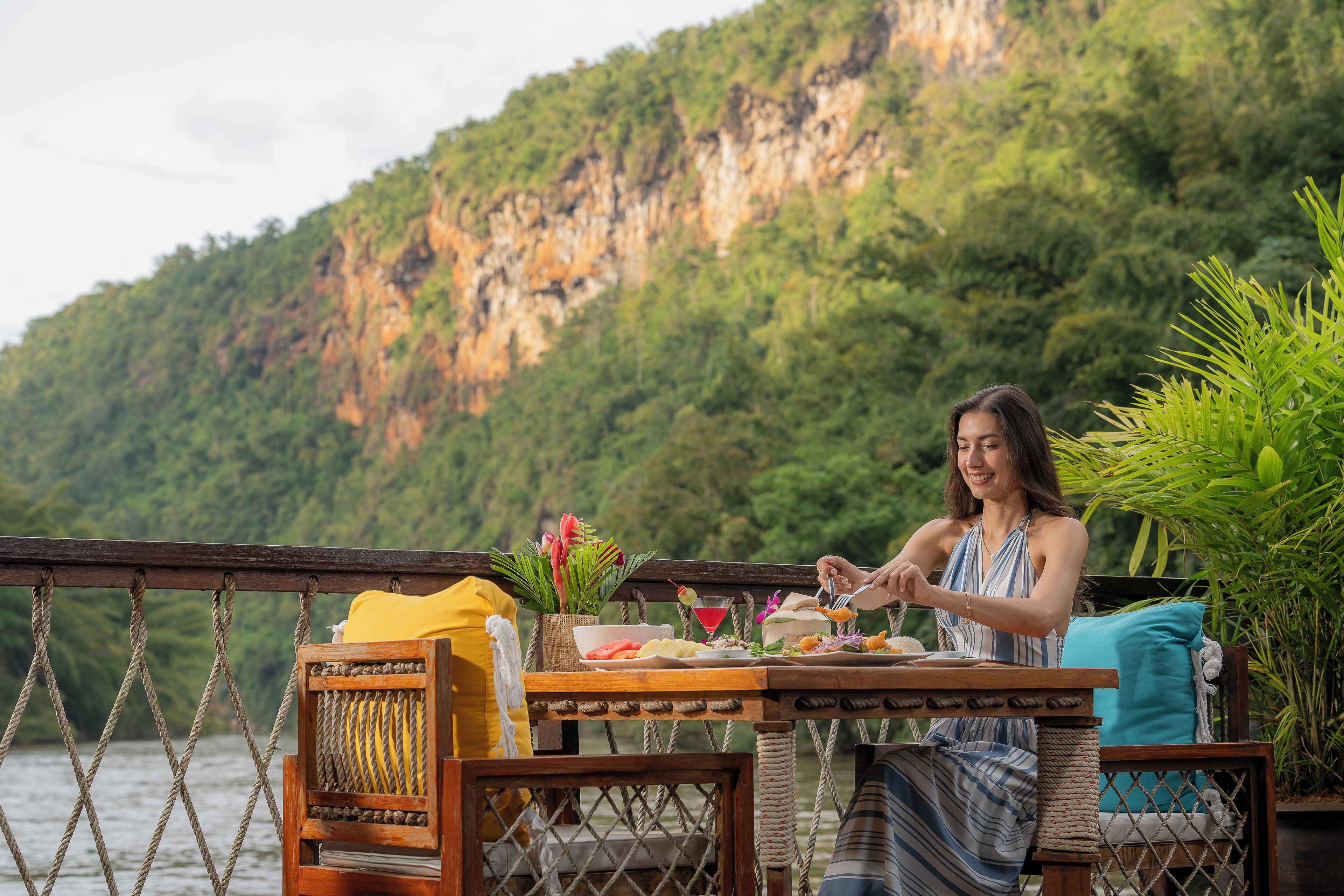 A dining area with a table set for two, overlooking a body of water and a mountainous landscape.