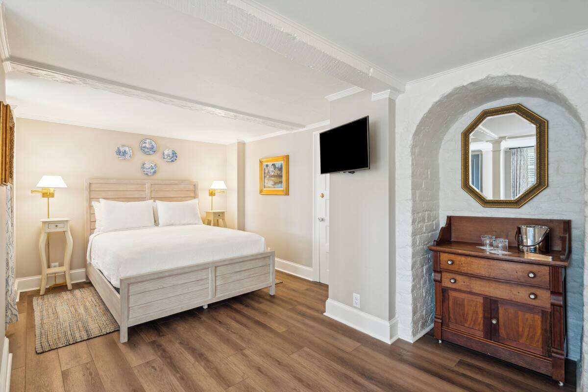 A hotel room with a wooden bed, a television, a mirror, and a wooden dresser.