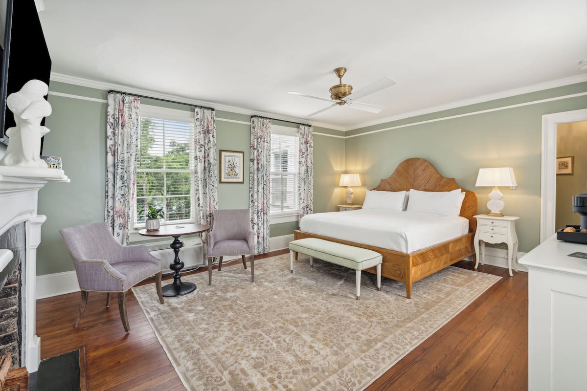 A bedroom with a large bed, a chair, a small table, and a fireplace.