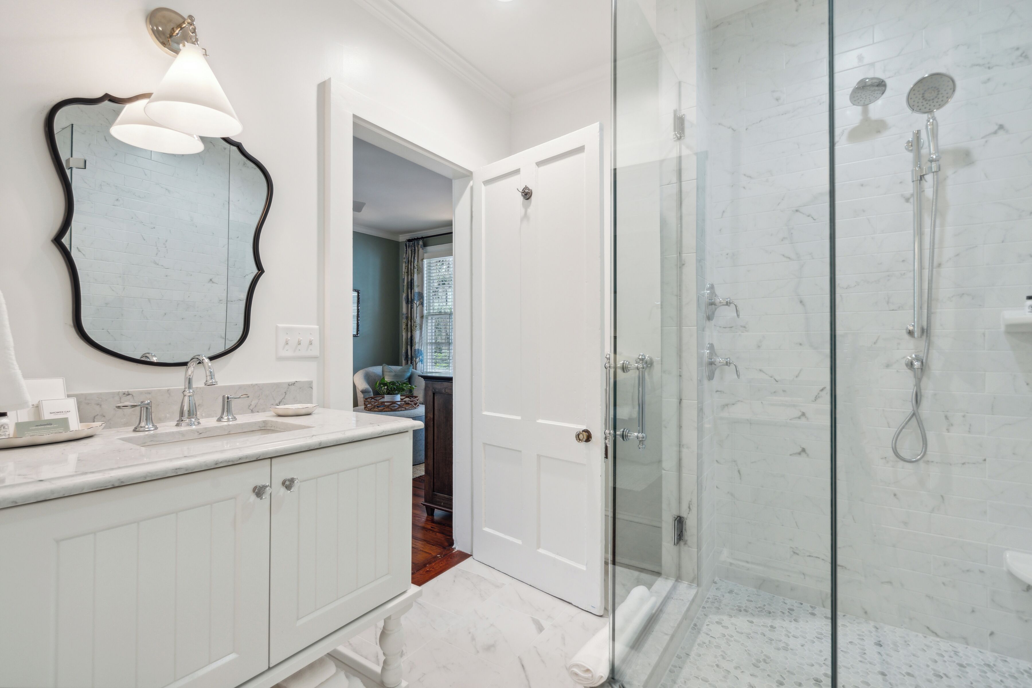 Een badkamer met een grote spiegel, een douche met glazen deur en een wit wastafelmeubel met een wastafel.