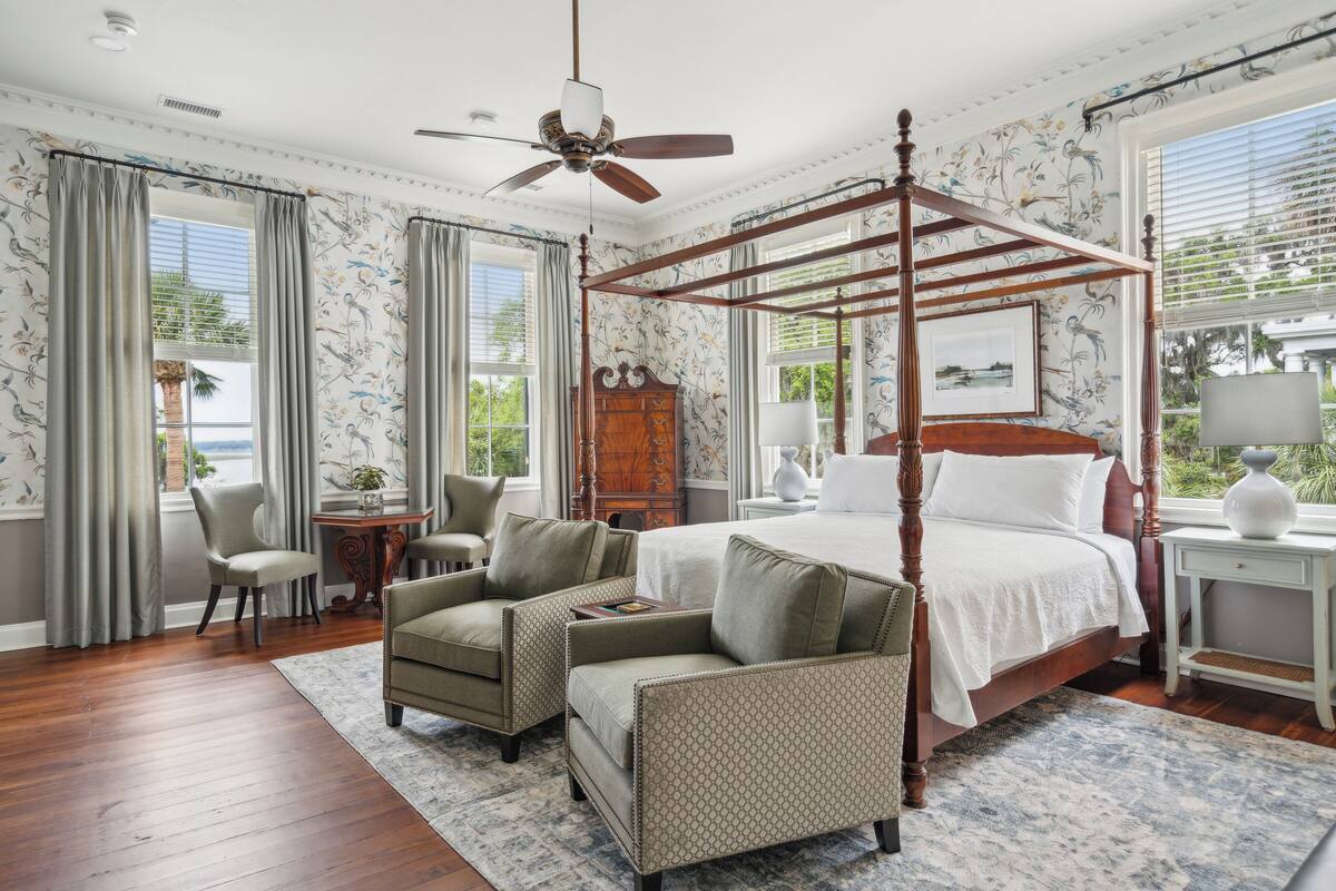 A spacious bedroom with a four-poster bed, a ceiling fan, and a view of the outdoors.