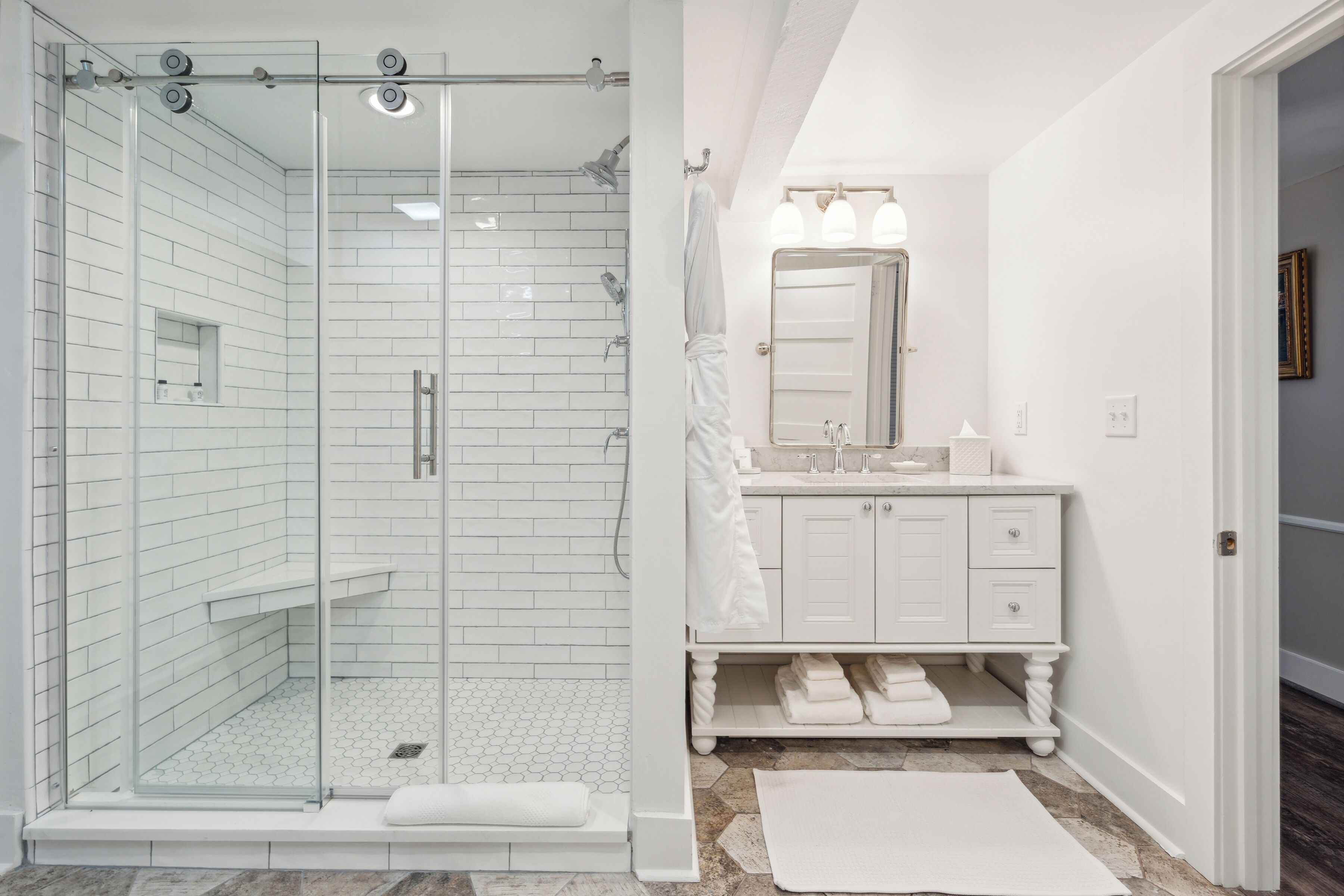 A modern bathroom with a glass-enclosed shower, white tiled walls, a vanity with a mirror, and a white sink.