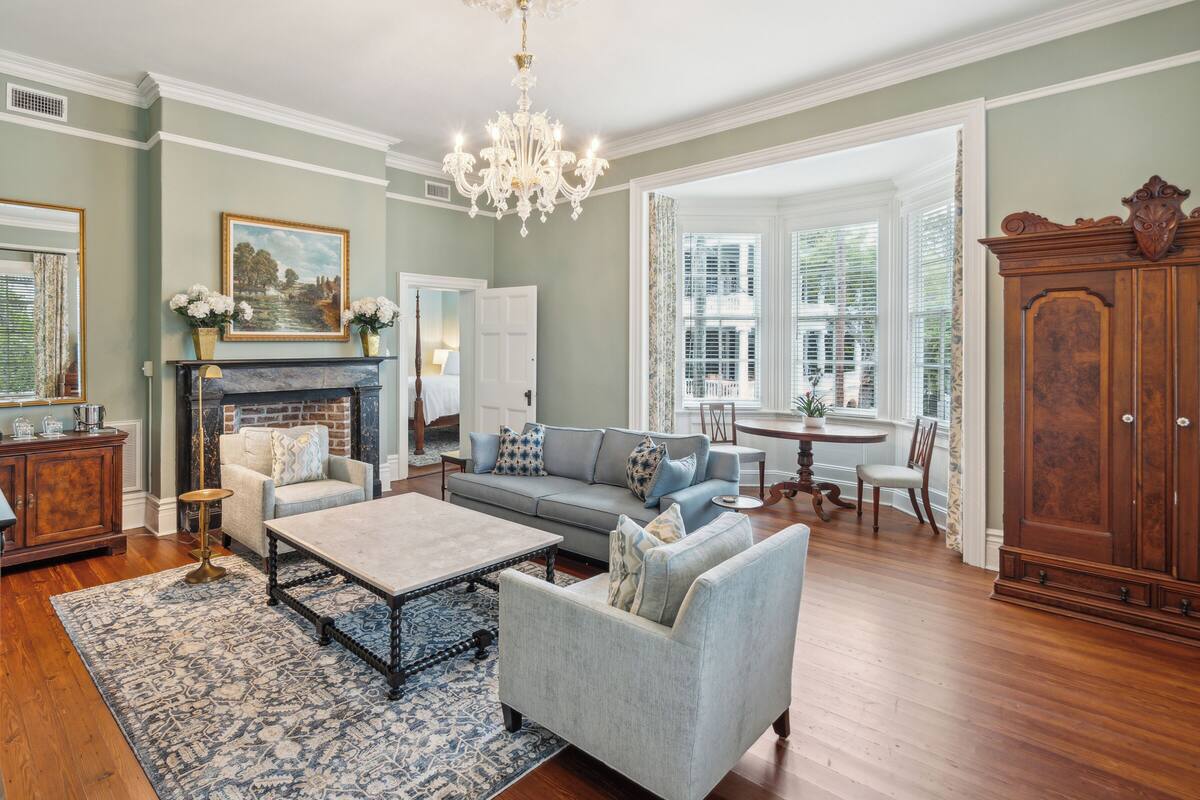 A spacious living room with a fireplace, a chandelier, and a large wooden cabinet.