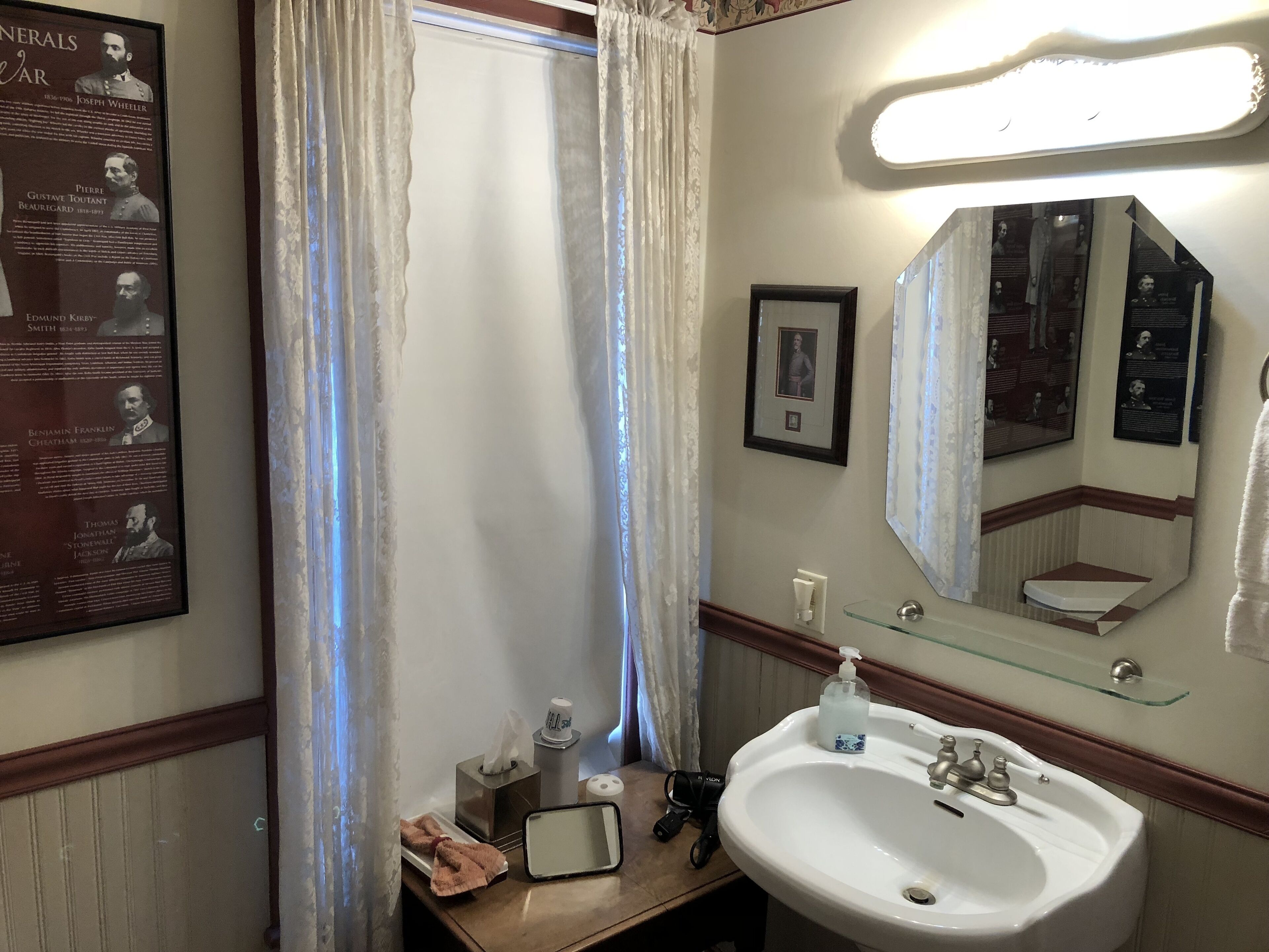 Un baño con un lavabo blanco, un espejo, un cuadro enmarcado y un póster en la pared.