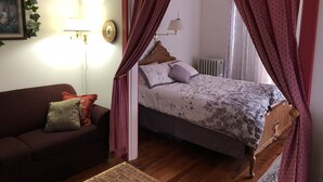 A bedroom with a bed, a wooden headboard, a nightstand, a red sofa, and a wall-mounted lamp. - Keller House (Centre Hall)