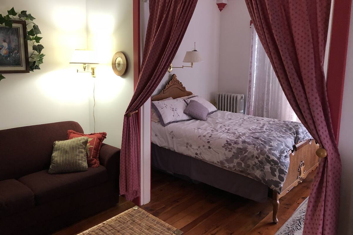 A bedroom with a bed, a wooden headboard, a nightstand, a red sofa, and a wall-mounted lamp.