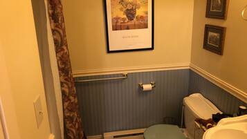 A bathroom with a toilet, a shower curtain, a radiator, and a framed picture on the wall.