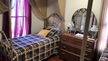 A four-poster bed with a patterned bedspread, a bedside table with a clock, and a mirror on the wall.