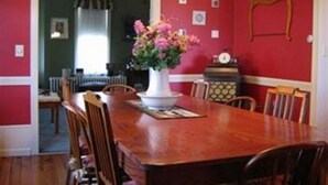 A dining room with a wooden table and chairs, a vase of flowers, and a clock on the wall. - Keller House (Centre Hall)