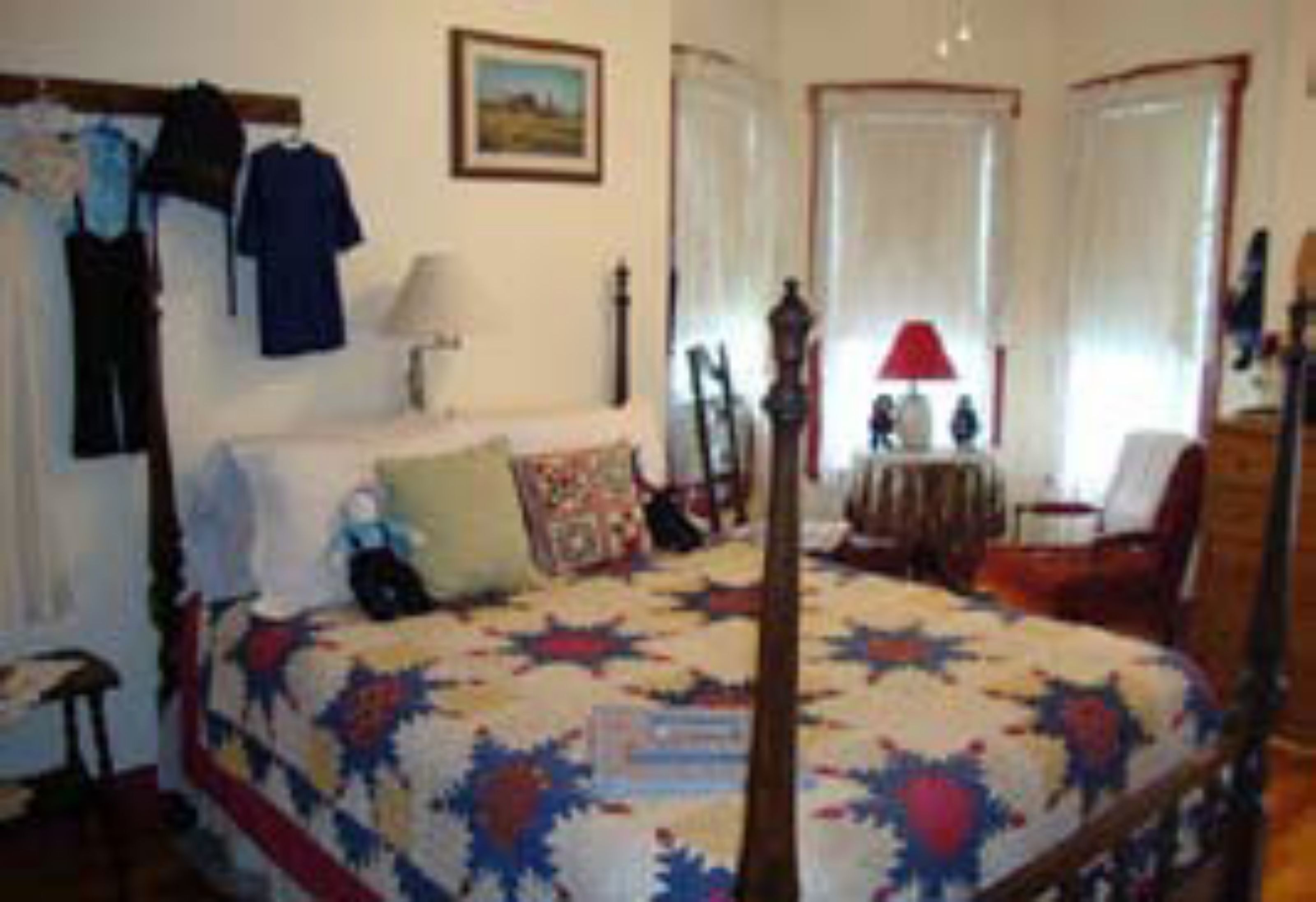 Un dormitorio con cama, mesita de noche, una silla, cómoda y ventana con cortinas.