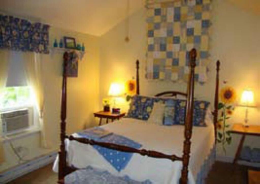 A four-poster bed with a quilt, a checkered wall hanging, and two bedside lamps.