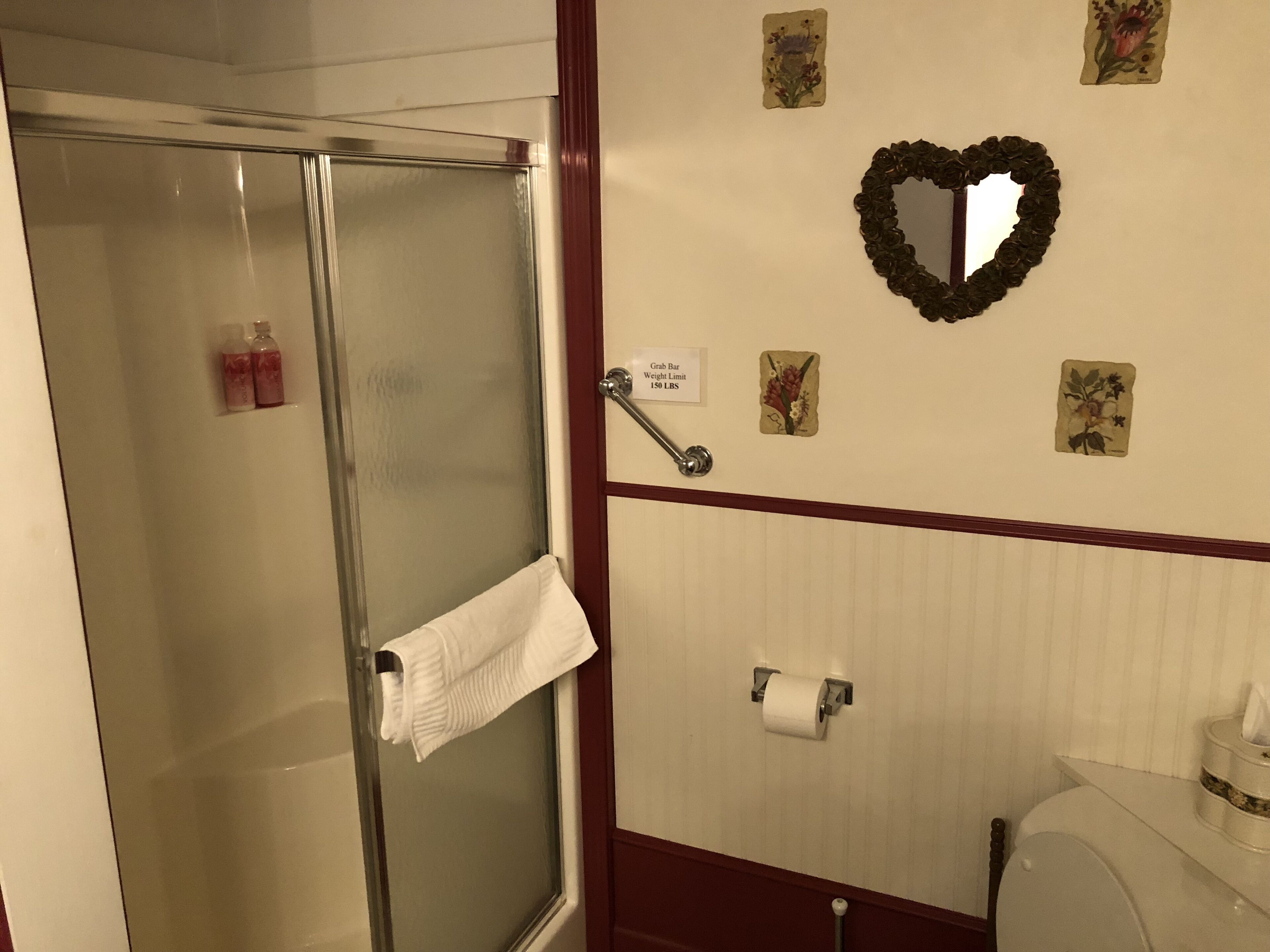 A bathroom with a glass shower door, a towel rack, a toilet paper holder, and decorative wall art.