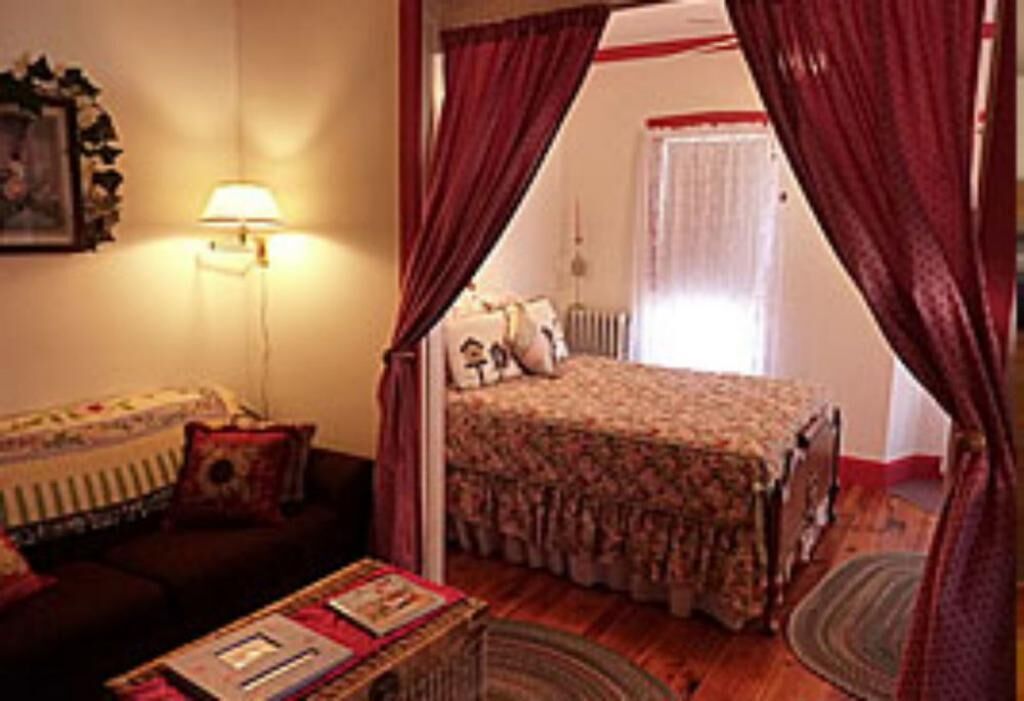 Un dormitorio acogedor con cama, mesita de noche, lámpara y ventana con cortinas.